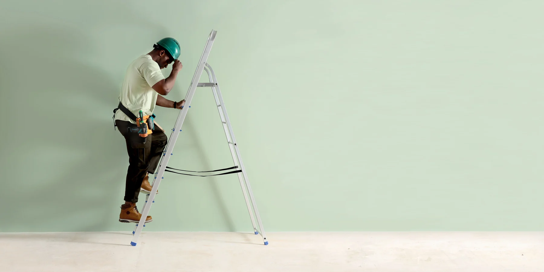 Construction worker climbing ladder against light green wall