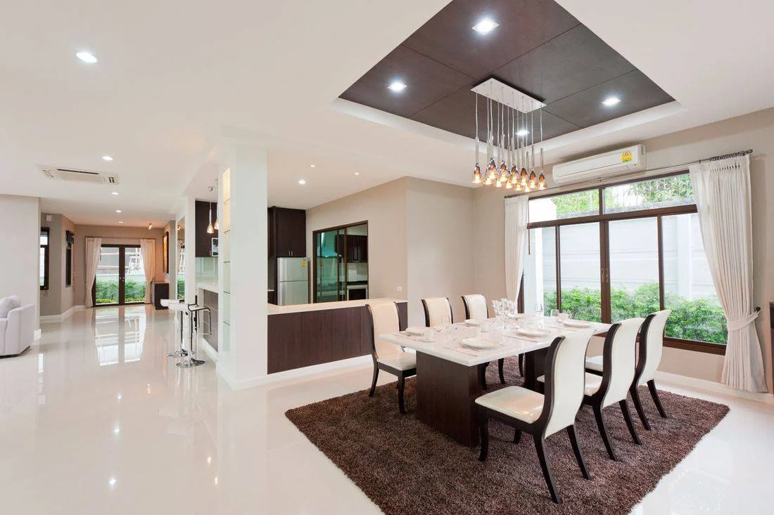 Modern dining room with white marble table, cream upholstered chairs, dark wood accents, and pendant lighting
