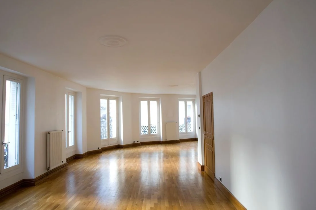 Empty living room with hardwood floors, multiple windows, and white walls