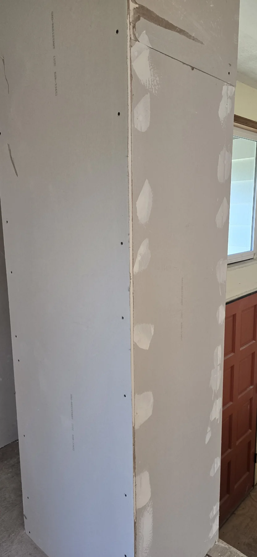 Drywall panels with joint compound patches and fastener holes in interior room construction