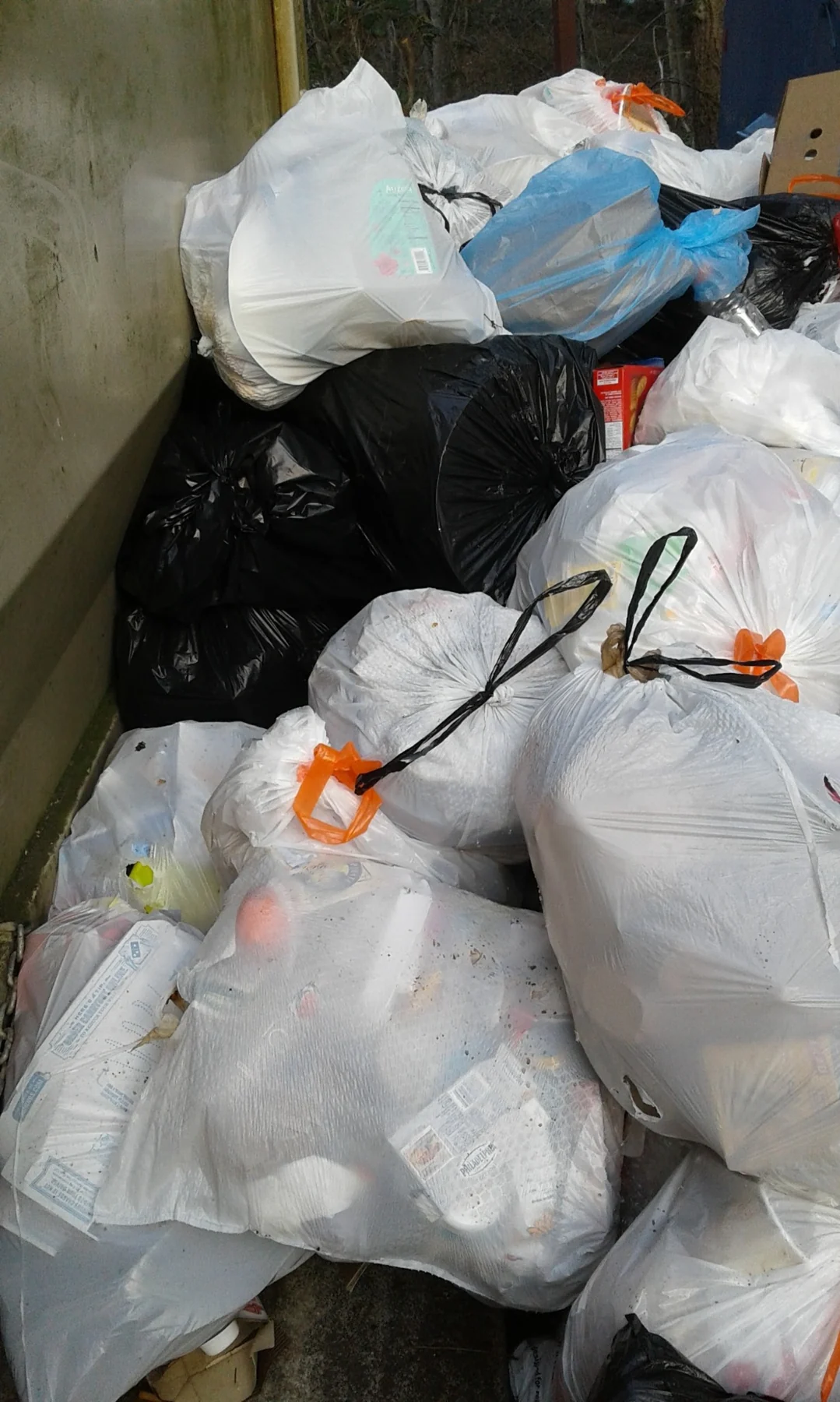 Multiple white and black garbage bags stacked in a pile with orange zip ties