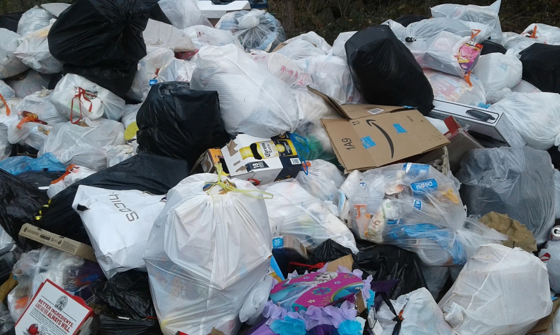 Large pile of mixed waste including plastic bags, cardboard boxes, and household items accumulated outdoors