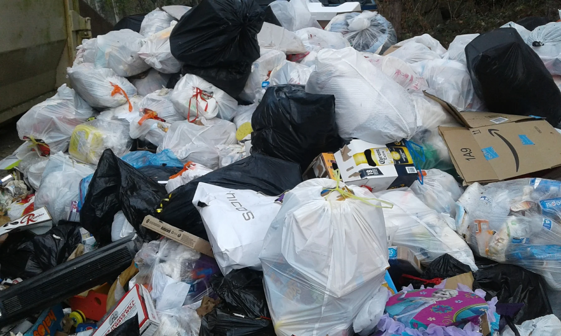 Large pile of mixed trash and recyclables including plastic bags, cardboard boxes, and household waste