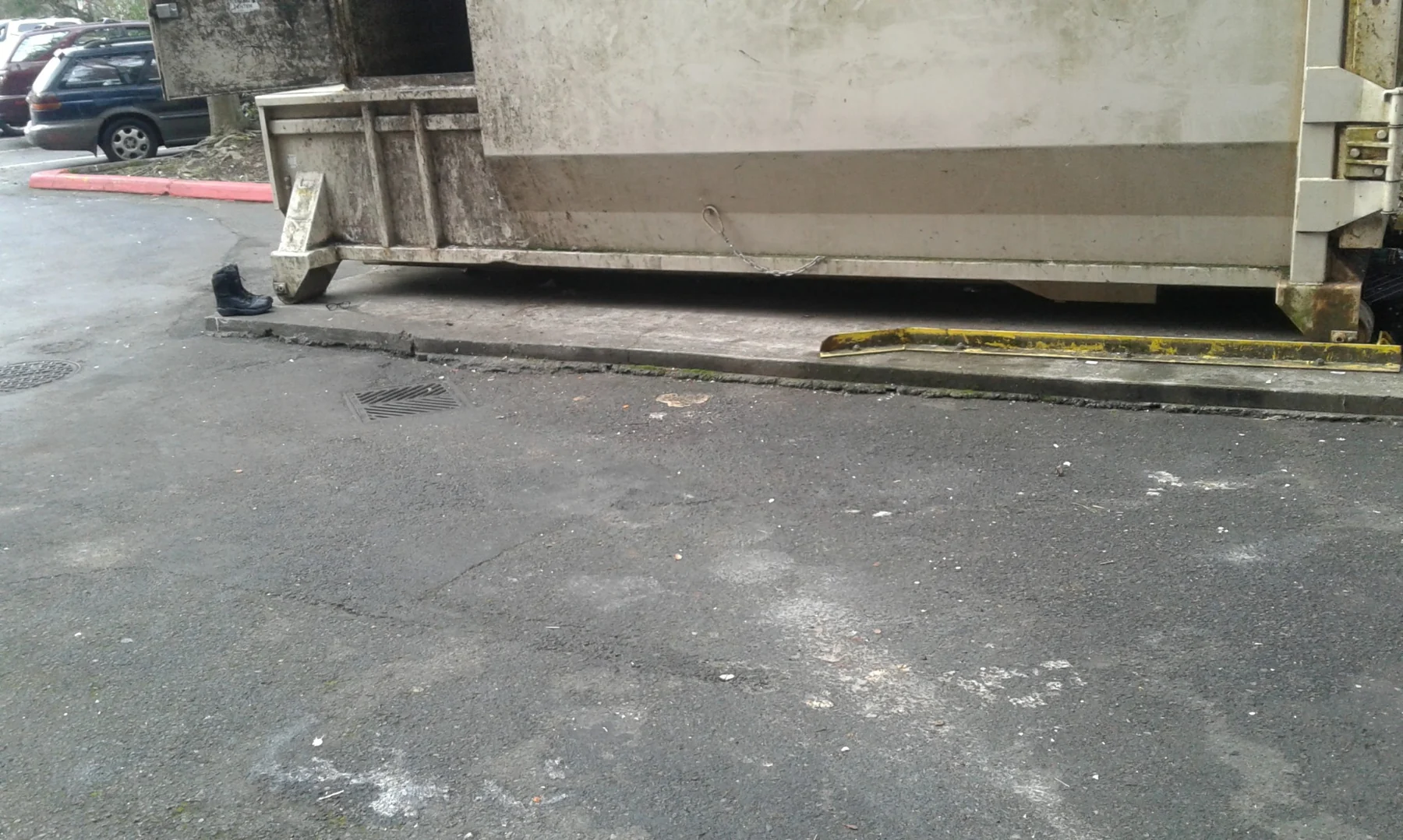 Concrete parking area with dumpster, metal ramp, and parked car in background