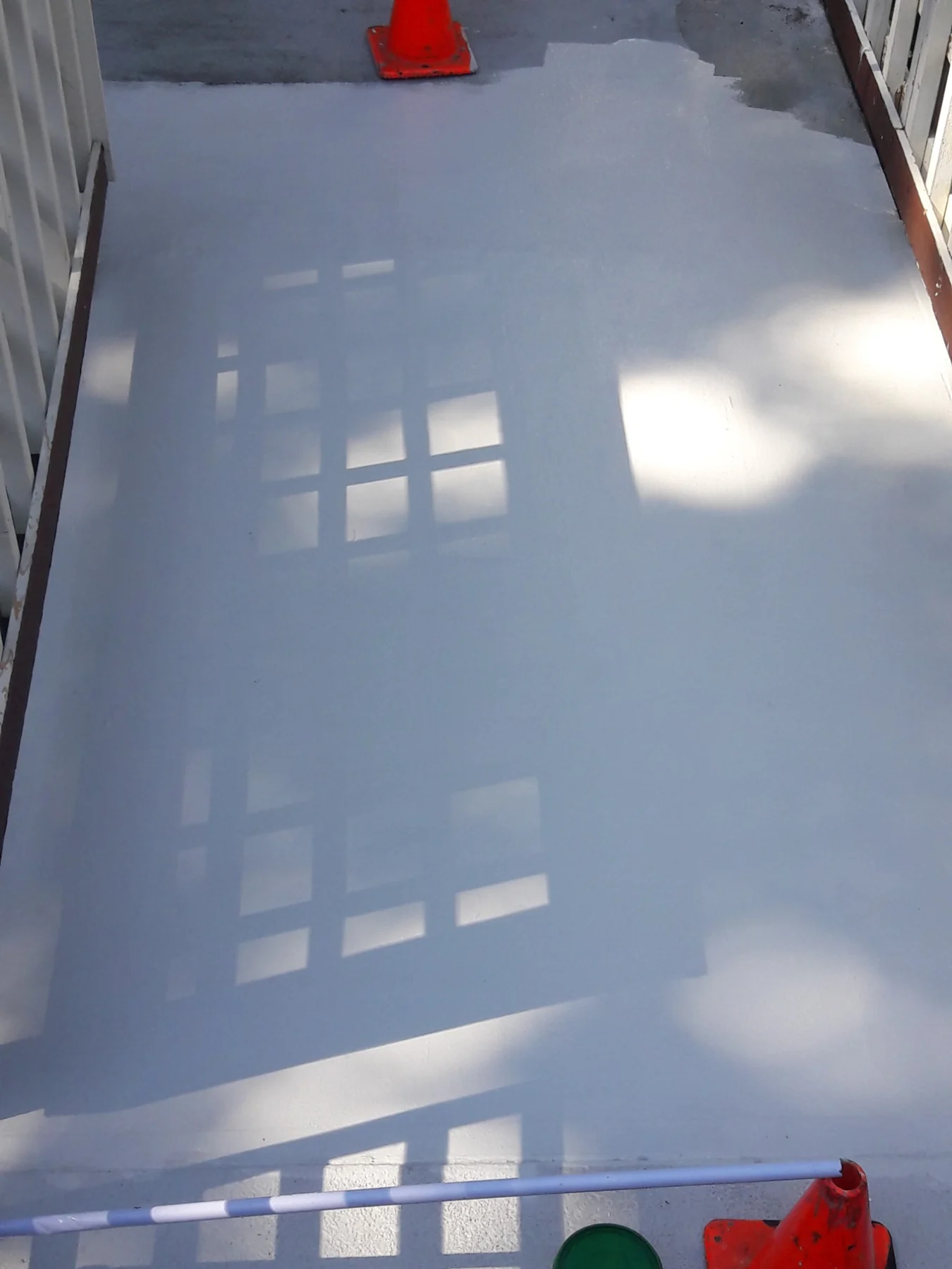 Flat rooftop surface with window shadows and red traffic cone