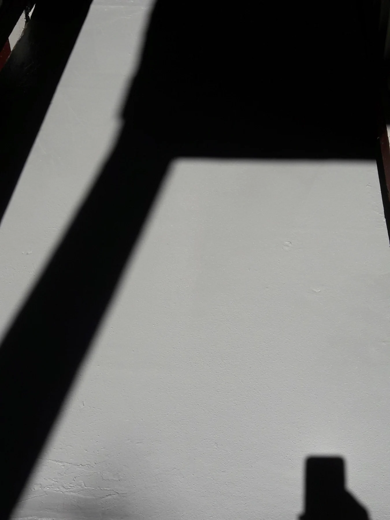 Sunlight casting sharp shadows on a white textured wall