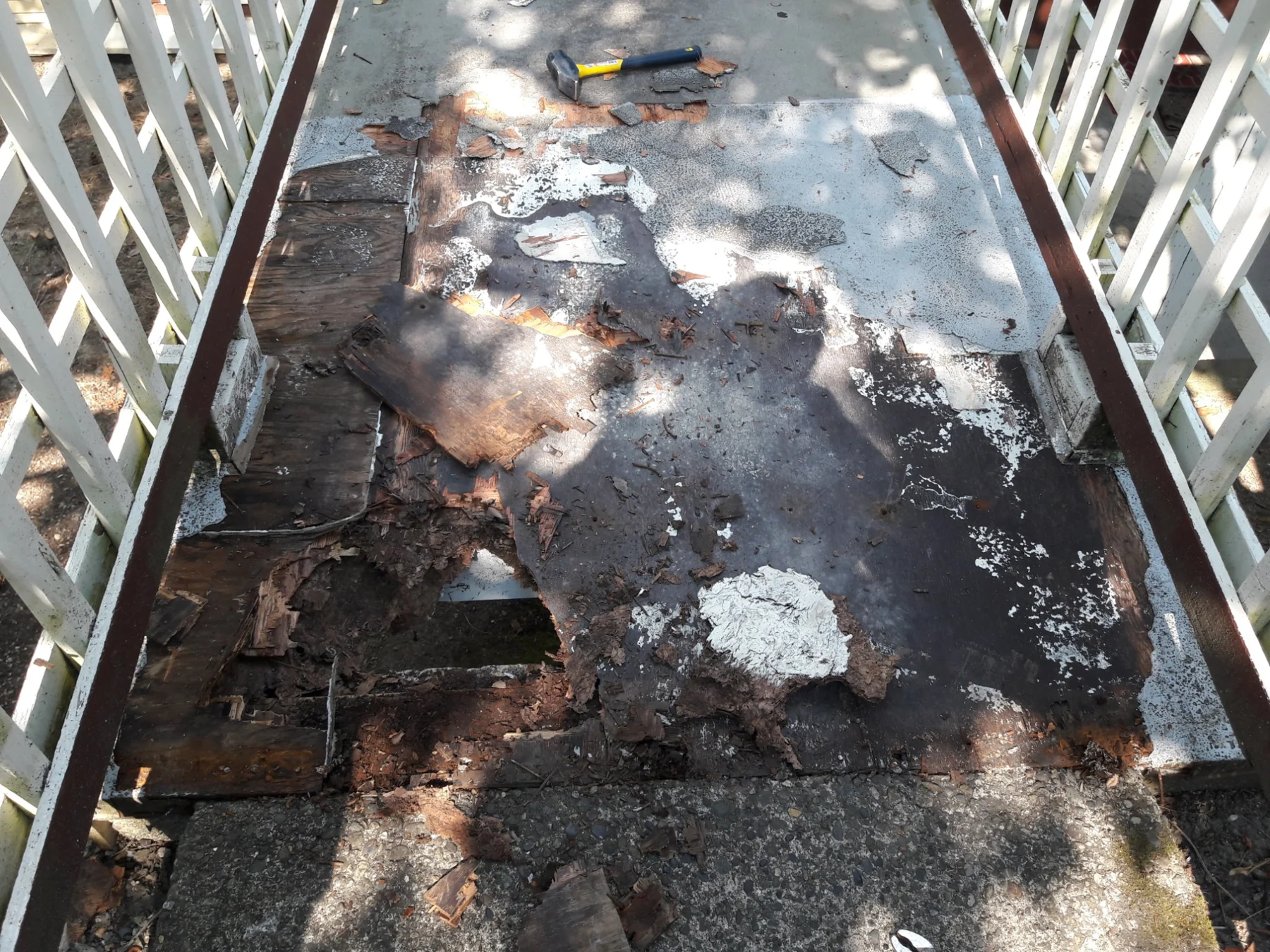 Deteriorated flat roof with peeling paint, exposed wood, rust stains, and a hammer tool visible