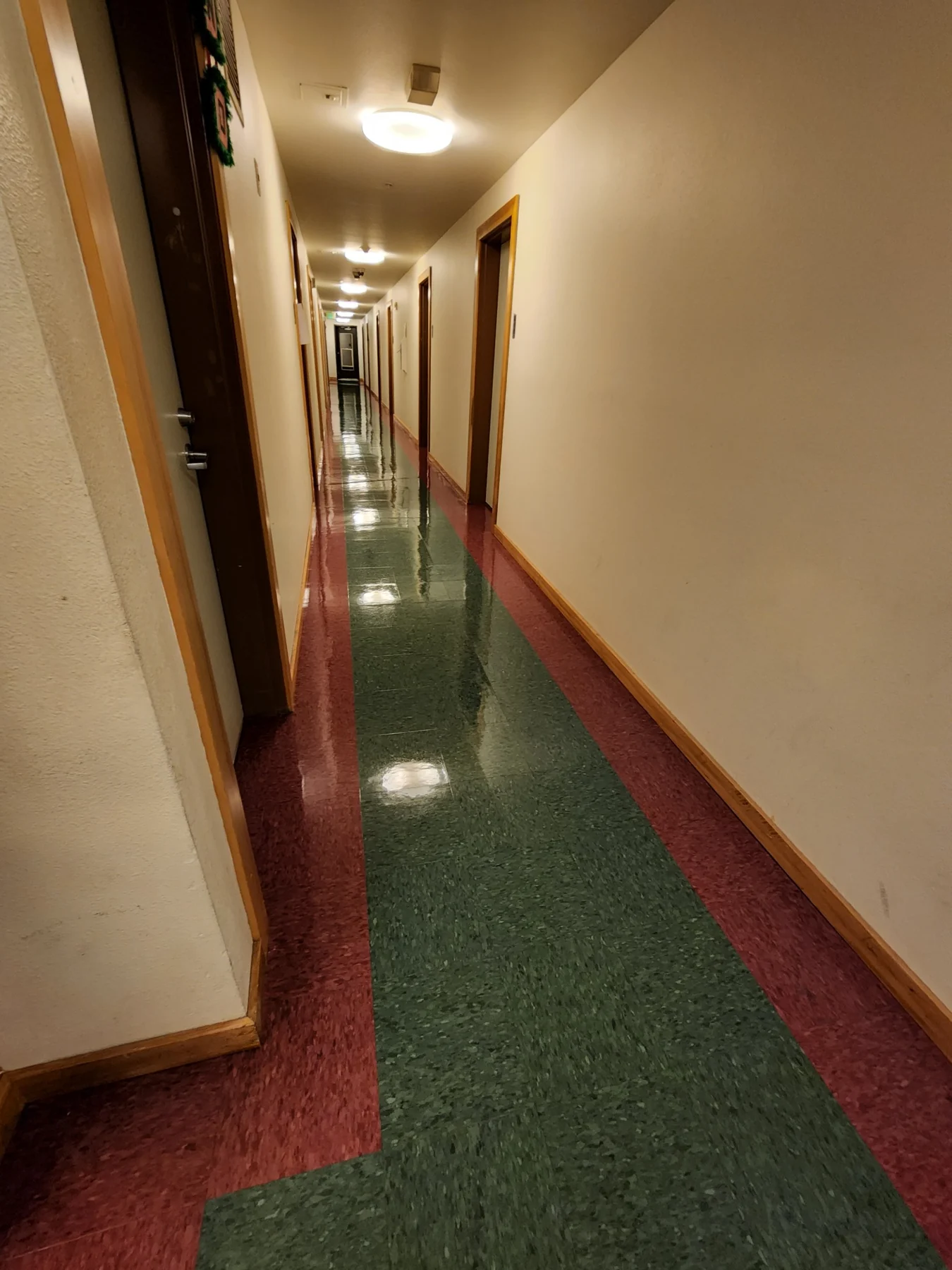 Long hallway with red and green striped flooring, white walls, and recessed ceiling lights