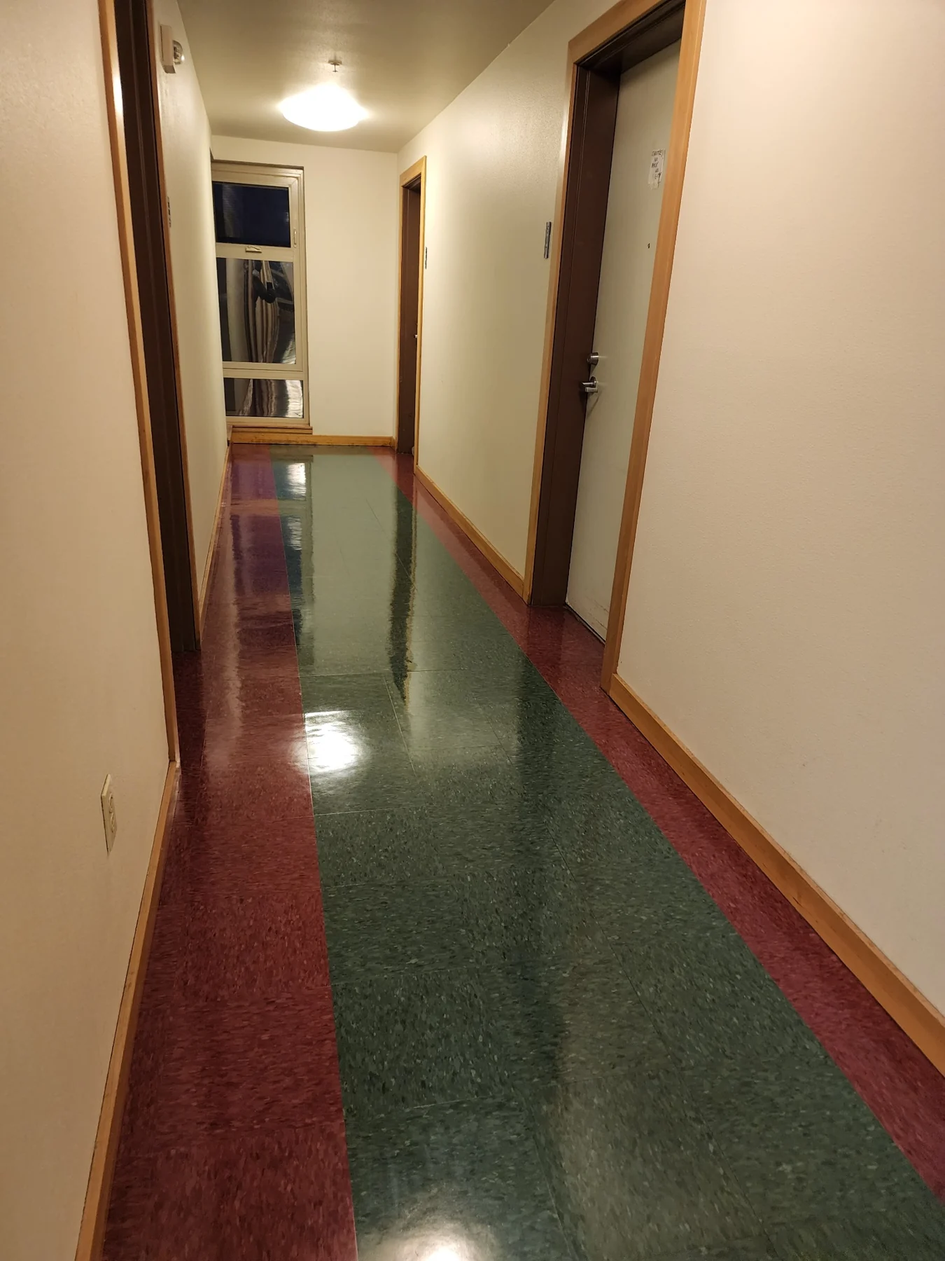 Long hallway with red and green striped flooring and wooden trim doors