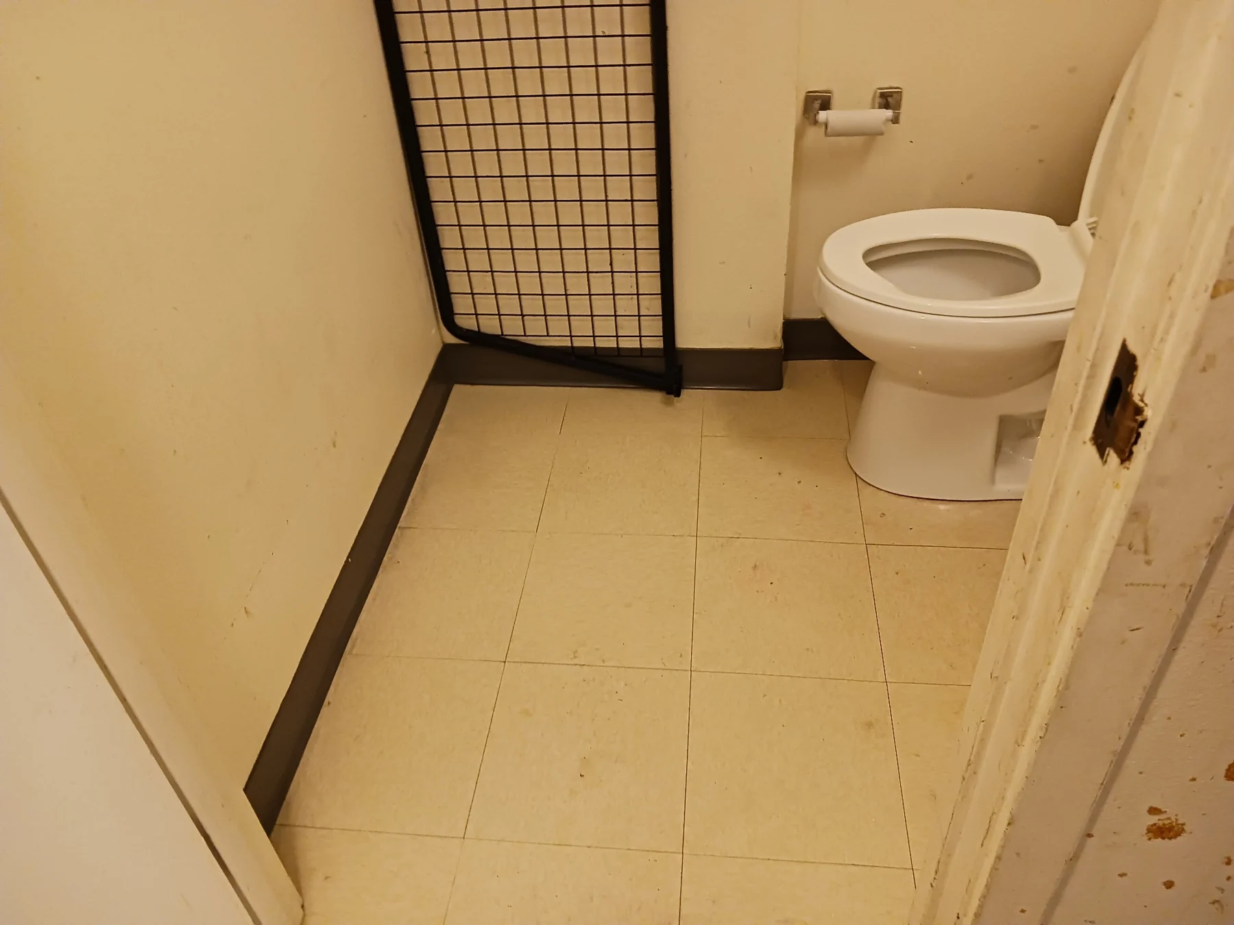 Empty bathroom with white toilet, beige tile floor, and metal gate barrier