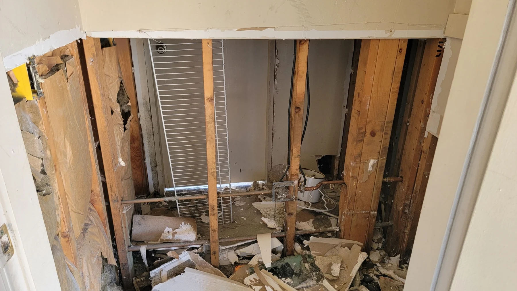 Interior wall cavity showing exposed wooden studs, debris, and deteriorated drywall during renovation