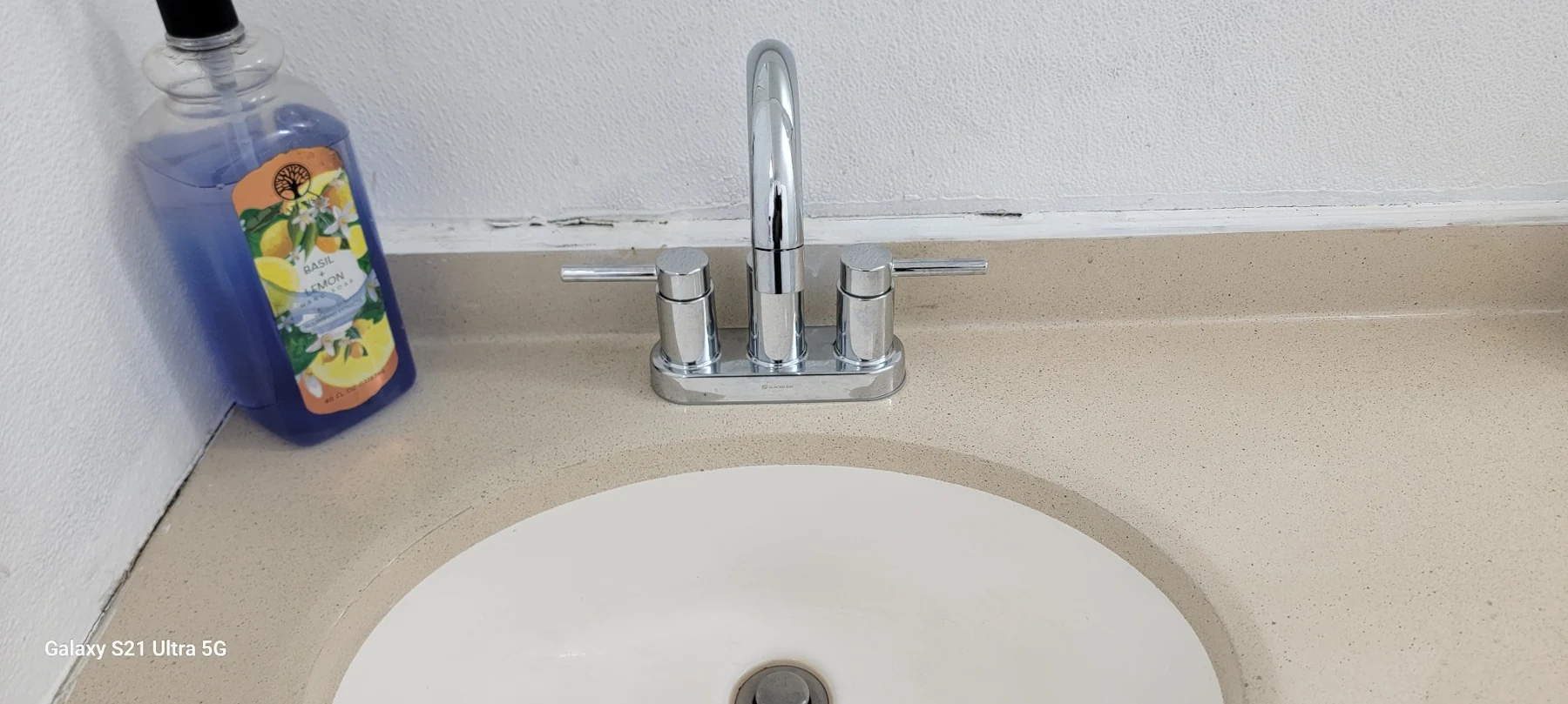 Modern bathroom sink with chrome faucet, beige countertop, and basil lemon soap bottle